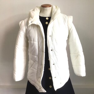 May include: A white puffer jacket with a hood and a button closure. The jacket has a quilted design and is made of a lightweight fabric.