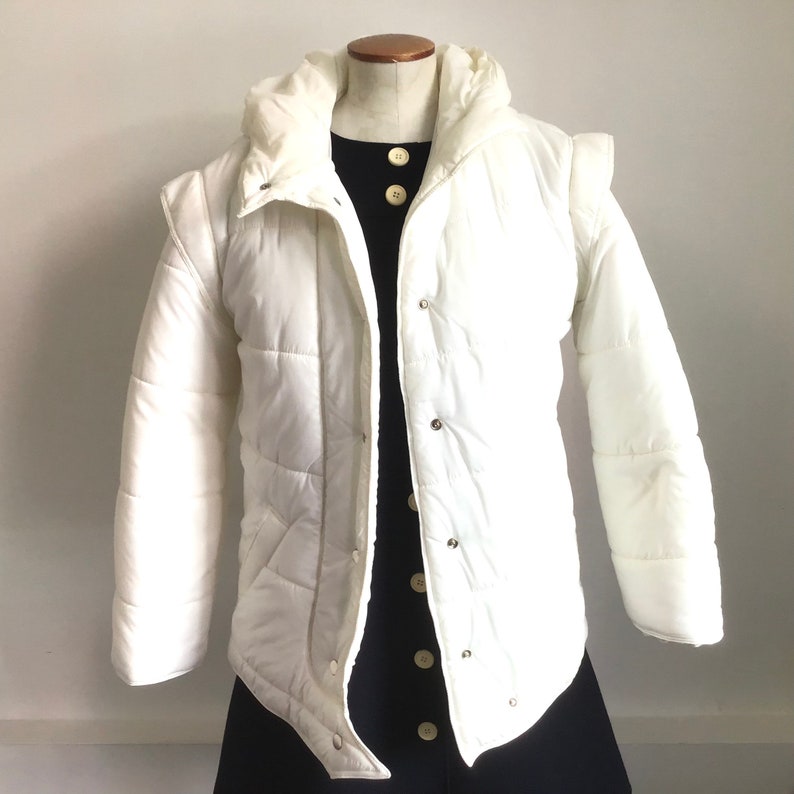 May include: A white puffer jacket with a hood and a button closure. The jacket has a quilted design and is made of a lightweight fabric.
