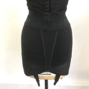 Puede incluir: Faja negra de cintura alta con un panel de malla y seis ligas. La faja tiene una textura lisa y acanalada y una pierna de corte alto.