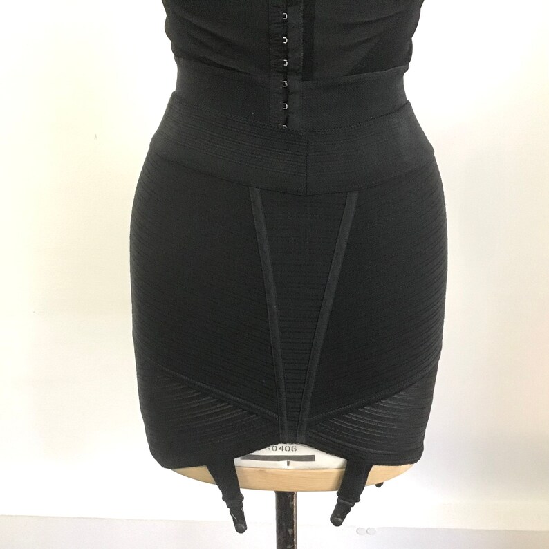 Puede incluir: Faja negra de cintura alta con un panel de malla y seis ligas. La faja tiene una textura lisa y acanalada y una pierna de corte alto.