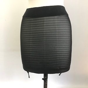 Puede incluir: Falda negra transparente con estampado de rayas y cintura negra. La falda tiene tirantes ajustables.