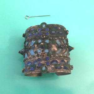 May include: A silver bracelet with blue, green, and white enamel detailing. The bracelet has a geometric design and is decorated with small spikes.