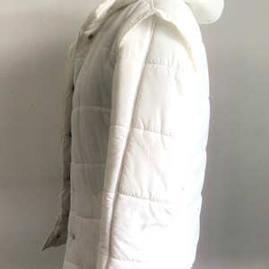 May include: A white hooded puffer jacket with a quilted design. The jacket has a zipper closure and snap buttons.