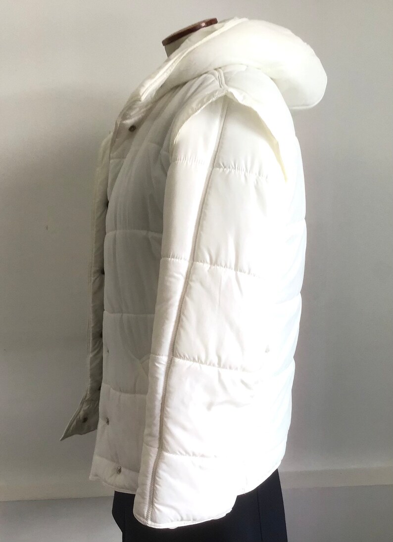 May include: A white hooded puffer jacket with a quilted design. The jacket has a zipper closure and snap buttons.