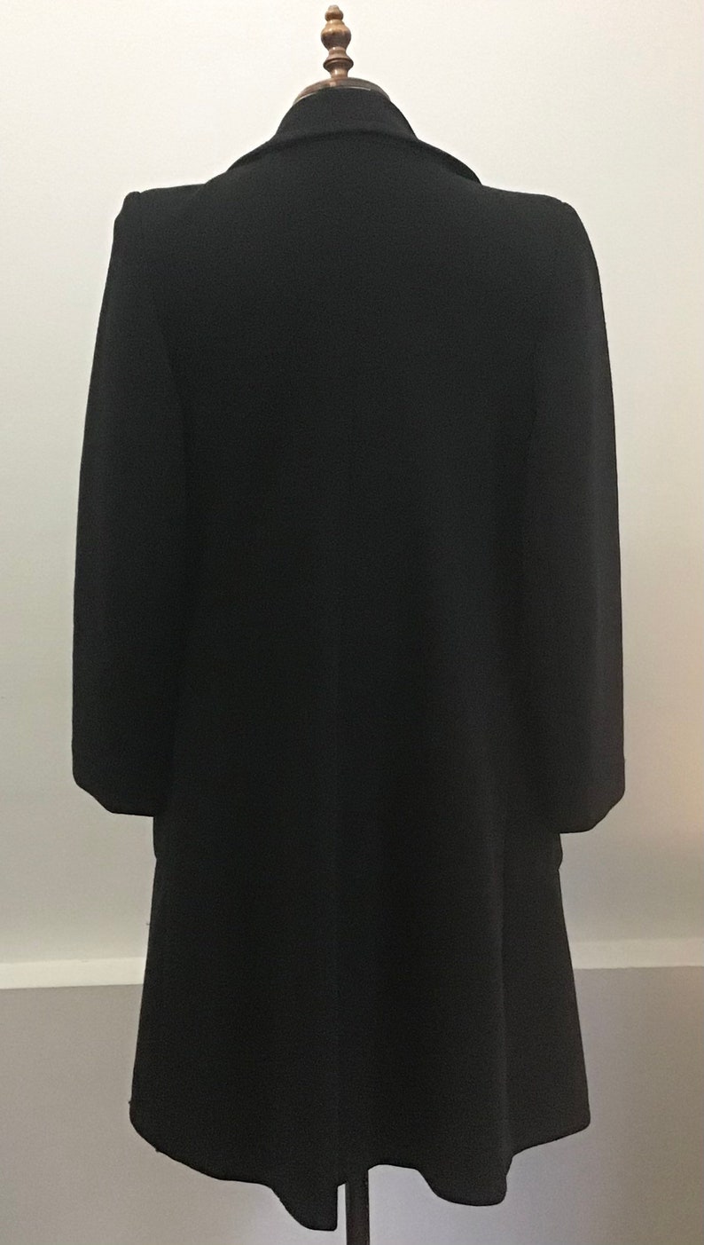 Pu&ograve; includere: Un cappotto di lana nero con un colletto classico e maniche lunghe. Il cappotto &egrave; sagomato e ha una silhouette aderente.