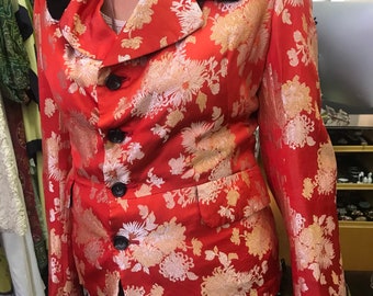 May include: A red blazer with a floral pattern in gold and cream. The blazer has a black collar and black buttons. The jacket is tailored with a classic fit.