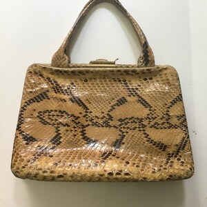 May include: A vintage handbag made of brown snakeskin with a gold clasp.