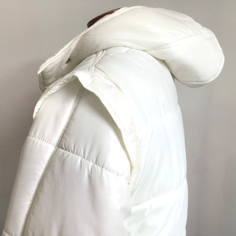 May include: White puffer jacket with a hood. The jacket has a quilted design and a zipper closure.