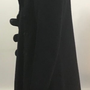 Pu&ograve; includere: Un cappotto nero a maniche lunghe con chiusura a doppio petto e bottoni.