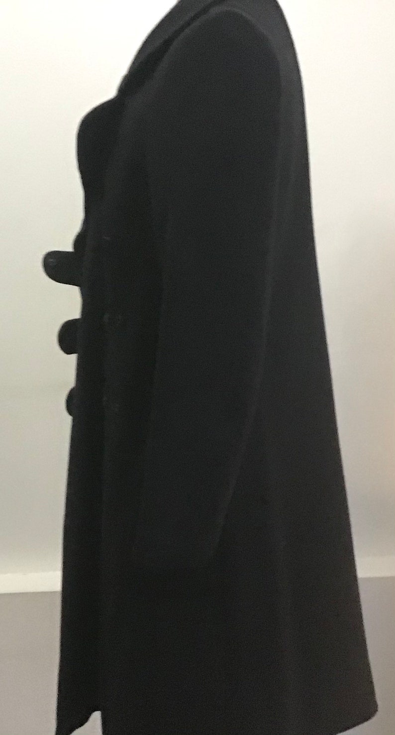 Pu&ograve; includere: Un cappotto nero a maniche lunghe con chiusura a doppio petto e bottoni.