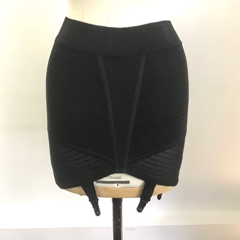 Puede incluir: Prenda negra, de canal&eacute;, de cintura alta, con un panel de malla y seis ligas. La prenda est&aacute; en un maniqu&iacute;.