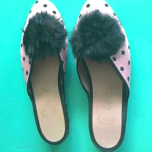 Könnte beinhalten: Ein Paar rosa und schwarze Polka-Dot-Hausschuhe mit schwarzen Pelzbommeln. Die Hausschuhe haben einen schwarzen Besatz an den Rändern und eine schwarze Ledersohle.