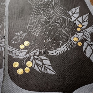 May include: A dark gray fabric panel featuring a detailed white illustration of a bird perched on a branch with leaves and golden berries. The bird's feathers and eye are intricately drawn. The panel has a textured appearance.