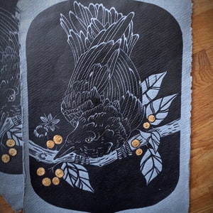 May include: Black and white illustration of a raven perched on a branch with leaves and golden berries. The artwork is set against a dark background with a light blue border, creating a striking contrast. The raven's feathers are detailed.