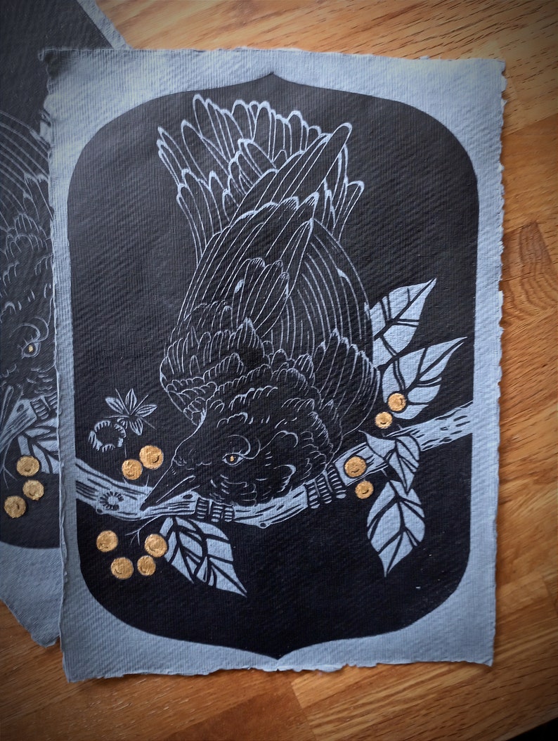 May include: Black and white illustration of a raven perched on a branch with leaves and golden berries. The artwork is set against a dark background with a light blue border, creating a striking contrast. The raven's feathers are detailed.