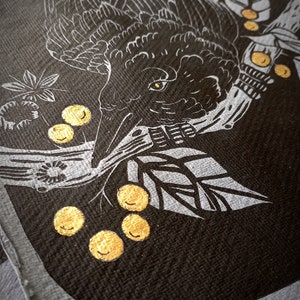 May include: A close-up of a black and white illustration of a crow with gold accents. The crow is perched on a branch with gold berries. The artwork is on a dark background.