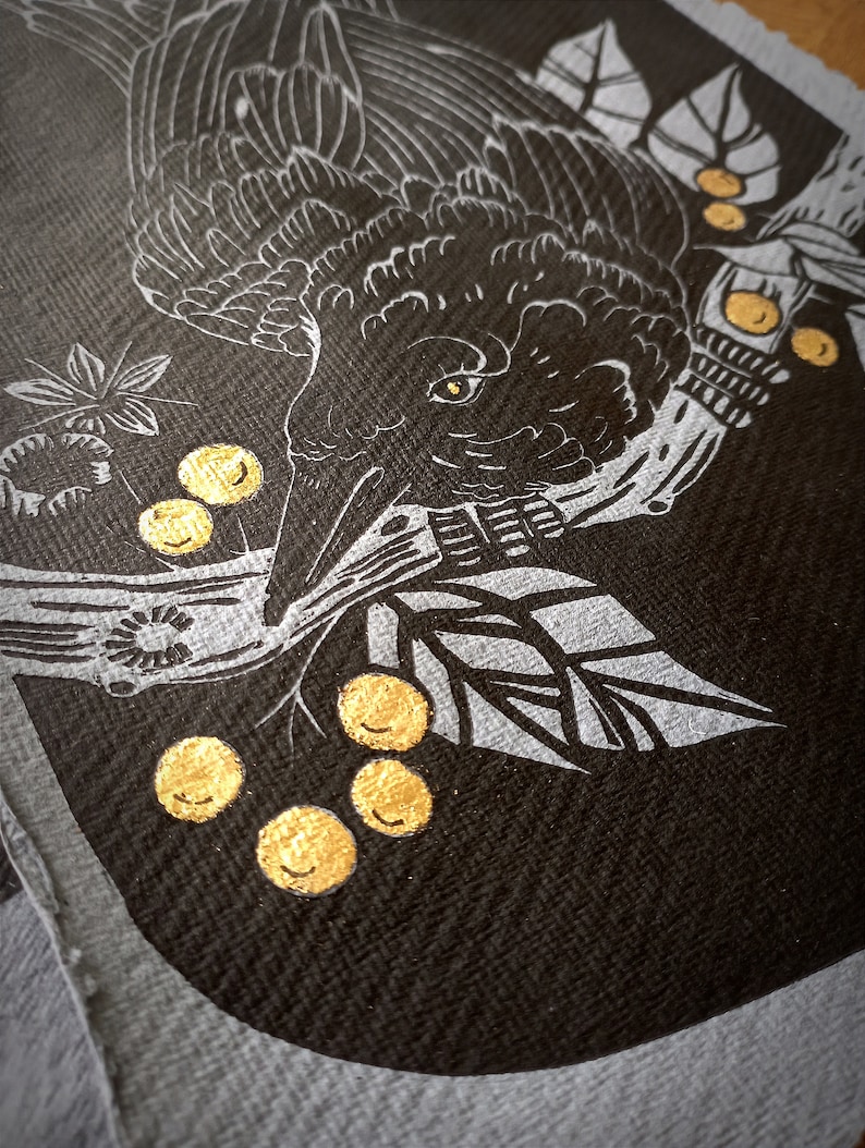 May include: A close-up of a black and white illustration of a crow with gold accents. The crow is perched on a branch with gold berries. The artwork is on a dark background.