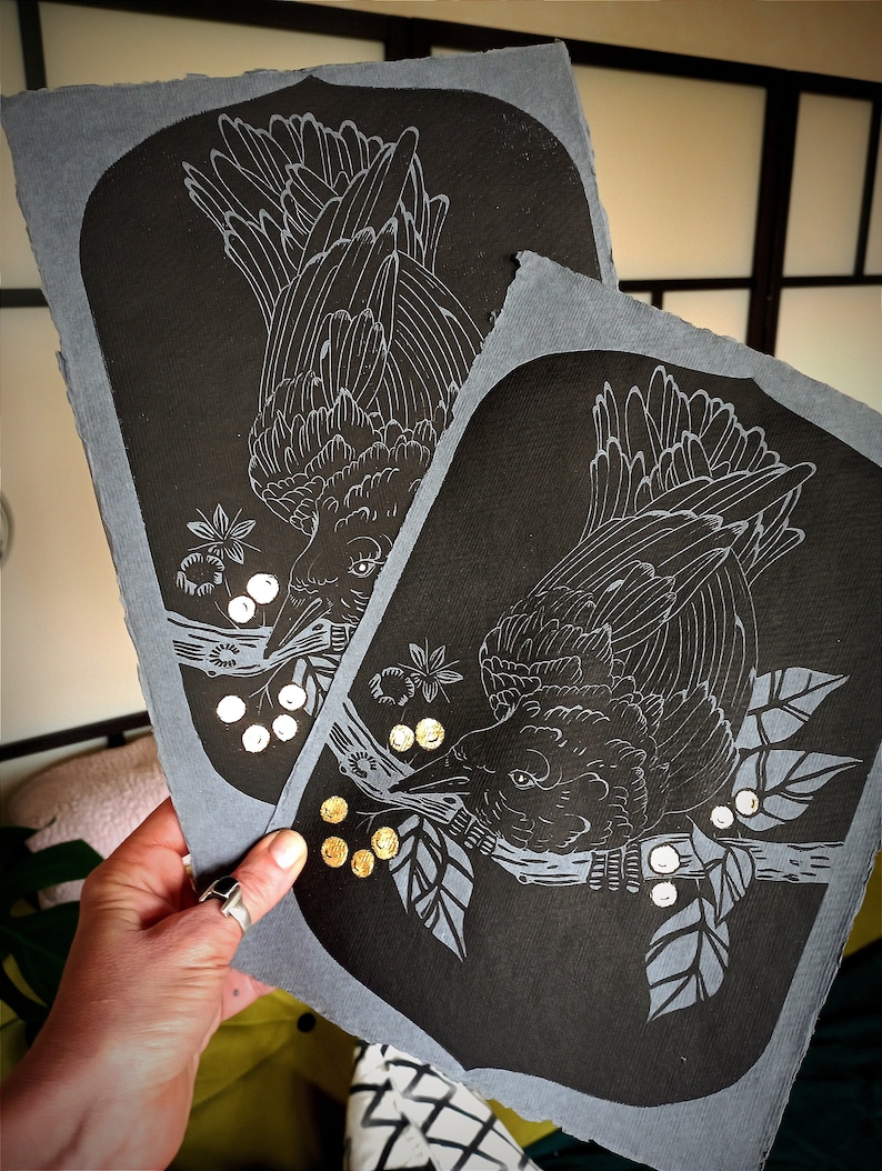 May include: Two black and gray art prints featuring a detailed illustration of a crow perched on a branch with berries. The crow is rendered in white lines against a black background. The prints have a gray border.