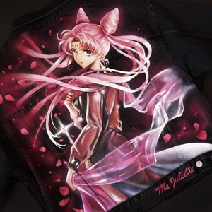 May include: A black denim jacket featuring a hand-painted image of a pink-haired anime character with a crown and a flowing pink cape. The character is holding a glowing pink object. The jacket has the text "Ms Juliette" on the bottom right corner.