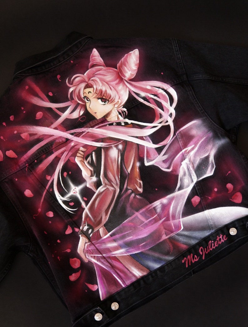 May include: A black denim jacket featuring a hand-painted image of a pink-haired anime character with a crown and a flowing pink cape. The character is holding a glowing pink object. The jacket has the text "Ms Juliette" on the bottom right corner.