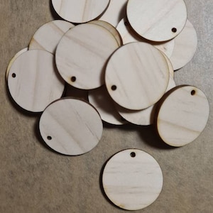 May include: A pile of 12 unfinished, round, wooden circles with a small hole in the centre. The circles are approximately 5 cm in diameter.