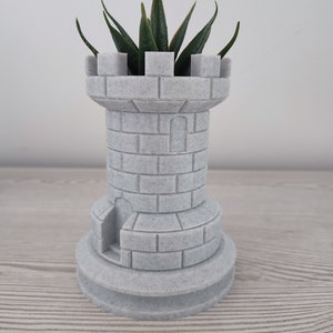 Puede incluir: Un macetero de cerámica blanco con forma de torre de castillo con una pequeña planta suculenta verde creciendo en su interior.