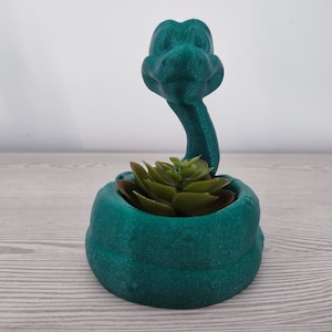 Pode incluir: Um vaso de cobra verde-azulado com uma planta suculenta dentro. O vaso de cobra é impresso em 3D e tem uma superfície texturizada.