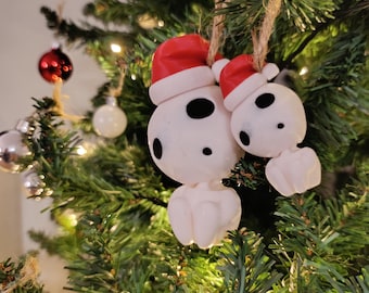 May include: Two white Christmas ornaments shaped like ghosts wearing red Santa hats. The ornaments are hanging from a green Christmas tree.