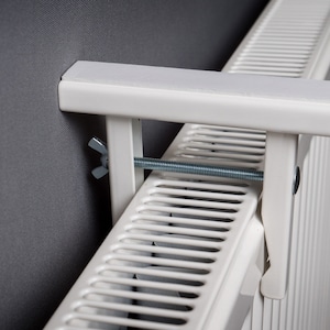 May include: White metal radiator bracket with a screw and a nut. The bracket is attached to a white radiator.