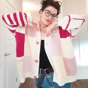 May include: A pink and white striped and checkered cardigan with a button closure. The cardigan is made of a soft, fuzzy yarn.