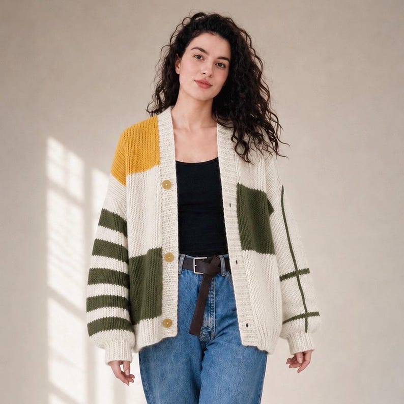 May include: A chunky knit cardigan featuring a color-blocked design in cream, mustard yellow, and olive green. The garment has a V-neckline, long sleeves with striped and grid patterns, and three round buttons down the front closure.