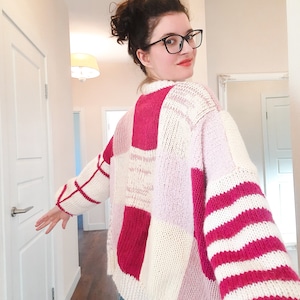 May include: A chunky knit sweater featuring a patchwork design of cream, bright pink, and light pink blocks. The sleeves display alternating horizontal stripes of cream and bright pink, while the body consists of large, solid-colored squares.
