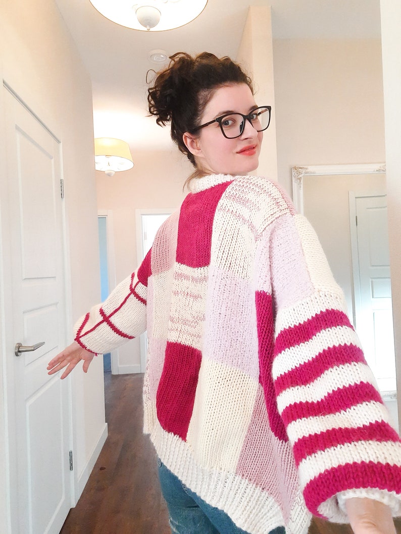 May include: A chunky knit sweater featuring a patchwork design of cream, bright pink, and light pink blocks. The sleeves display alternating horizontal stripes of cream and bright pink, while the body consists of large, solid-colored squares.