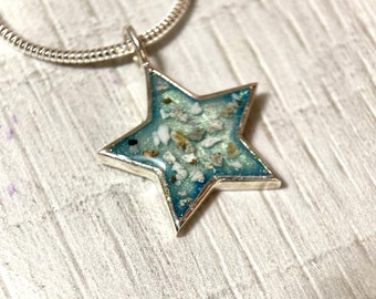 May include: A silver chain necklace with a star-shaped pendant. The pendant is filled with blue resin and contains small white and brown particles.