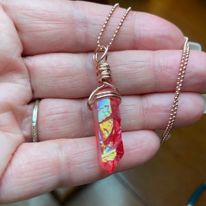 Può includere: Una collana con catena in oro rosa con un ciondolo in cristallo rosa iridescente avvolto in filo d'oro rosa.