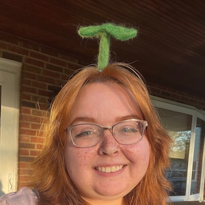Puede incluir: Una mujer con el pelo rojo que lleva gafas y un sombrero de fieltro verde en forma de hongo.