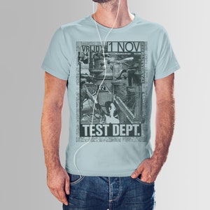 Könnte beinhalten: Hellblaues T-Shirt mit einer Schwarz-Weiß-Grafik. Die Grafik zeigt eine Collage von Industrie-Bildern und den Text "TEST DEPT." und "1 NOV". Das Shirt hat einen Rundhalsausschnitt und kurze Ärmel.