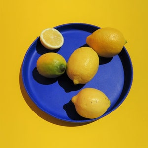 May include: Four lemons and a lemon wedge on a blue plate. The plate is on a yellow background.