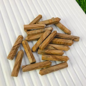 Puede incluir: Un montón de puntas de arenisca marrón y beige, también conocidas como madera petrificada, sobre una superficie blanca texturizada. Las puntas miden aproximadamente 2,5 a 5 cm de largo.