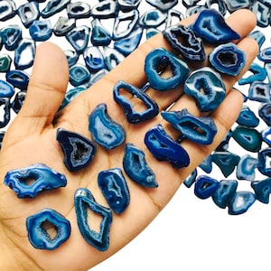 May include: A hand displays a selection of polished blue agate stones. The stones are in various shapes and sizes, with shades of deep and light blue. Some have a hollow centre, revealing a crystal-like interior.