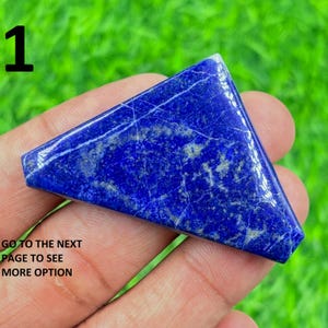 May include: A triangular, polished lapis lazuli gemstone with a deep blue colour and white veining. The stone is held in a hand against a blurred green background. The number "1" and text "GO TO THE NEXT PAGE TO SEE MORE OPTION" are visible.