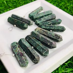 Może przedstawiać: Kolekcja fasetowanych zielonych i czerwonych kamieni szlachetnych z srebrnymi koralikami. Patyczki są ułożone wachlarzowo na białej powierzchni.