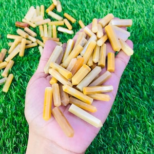 May include: A collection of yellow and white gemstone points, also known as citrine points, in a hand. The points are smooth and polished, and they are arranged in a random pattern.