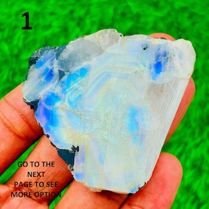 May include: A polished, iridescent moonstone slab with blue and white hues. The stone is held in a hand, with the text "1" in the upper left corner and "GO TO THE NEXT PAGE TO SEE MORE OPTION" in the lower left corner.