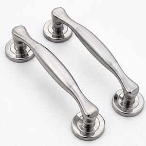 May include: Two silver-toned metal door handles with a smooth, curved design. Each handle features a central grip section that tapers toward the ends, connected to two circular mounting plates at the base with a polished, reflective finish.