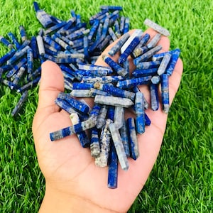 May include: A large pile of blue and white lapis lazuli gemstone points, also known as lapis lazuli wands, in a hand. The points are approximately 2.5-5 cm long.