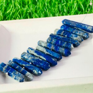 May include: A strand of twelve lapis lazuli gemstone beads, each carved into a long, pointed, rectangular shape. The beads are a deep blue with white streaks and are strung on a silver wire.