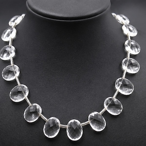 Peut inclure: Un collier composé d'une série de pierres précieuses transparentes, facettées et de forme ovale, enfilées ensemble. Chaque pierre est translucide et reflète la lumière à travers sa surface taillée, créant un motif uniforme.