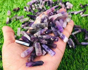May include: A hand holding a large pile of amethyst points. The points are various shades of purple and some have a slight shimmer.