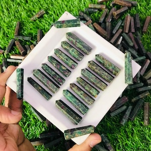 May include: A collection of green and red ruby zoisite gemstone points arranged in rows on a white surface. The points are approximately 2.5 cm in length.